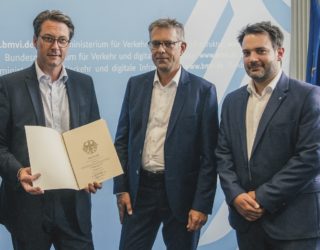 (v.l.n.r.): Bundesminister Andreas Scheuer übergibt Dr. Georg Klumpe, Zentralbereichsleiter Infrastruktur und Gert Messerschmidt, Referent Strategie für Sicherheit und Logistik von der Koelnmesse den neuen Förderbescheid.
