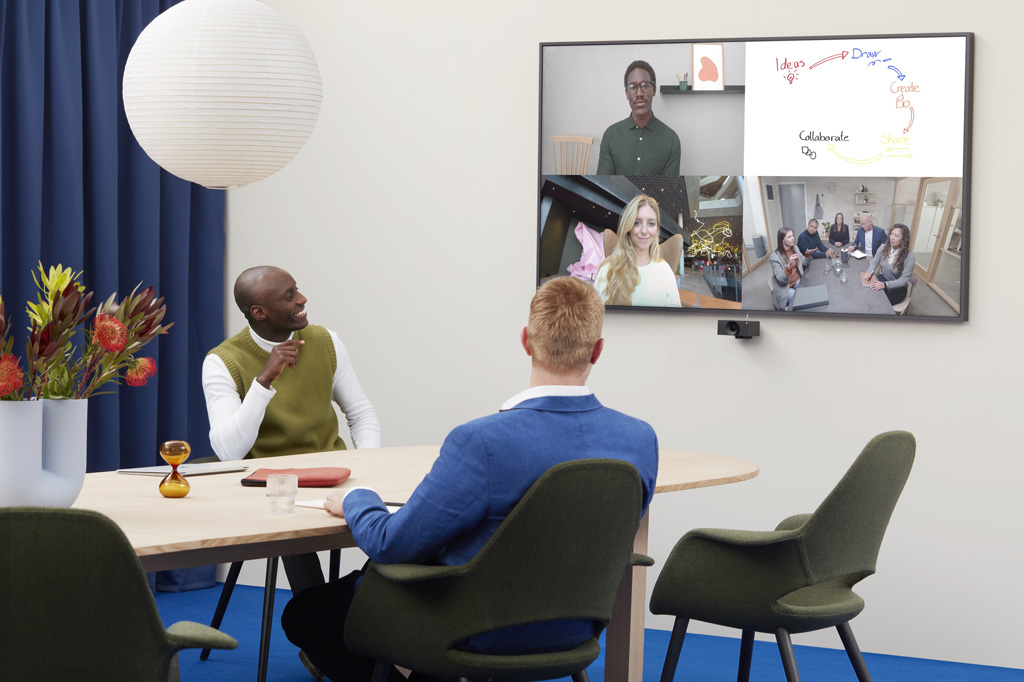 Zwei Männer in einem Konferenzraum betrachten einen anderen Mann per Videokonferenz