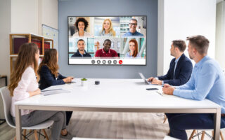 Personen in einem Konferenzraum halten eine Videokonferenz mit Leuten