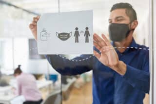 Mann hängt Zettel mit Hygiene-Hinweisen auf