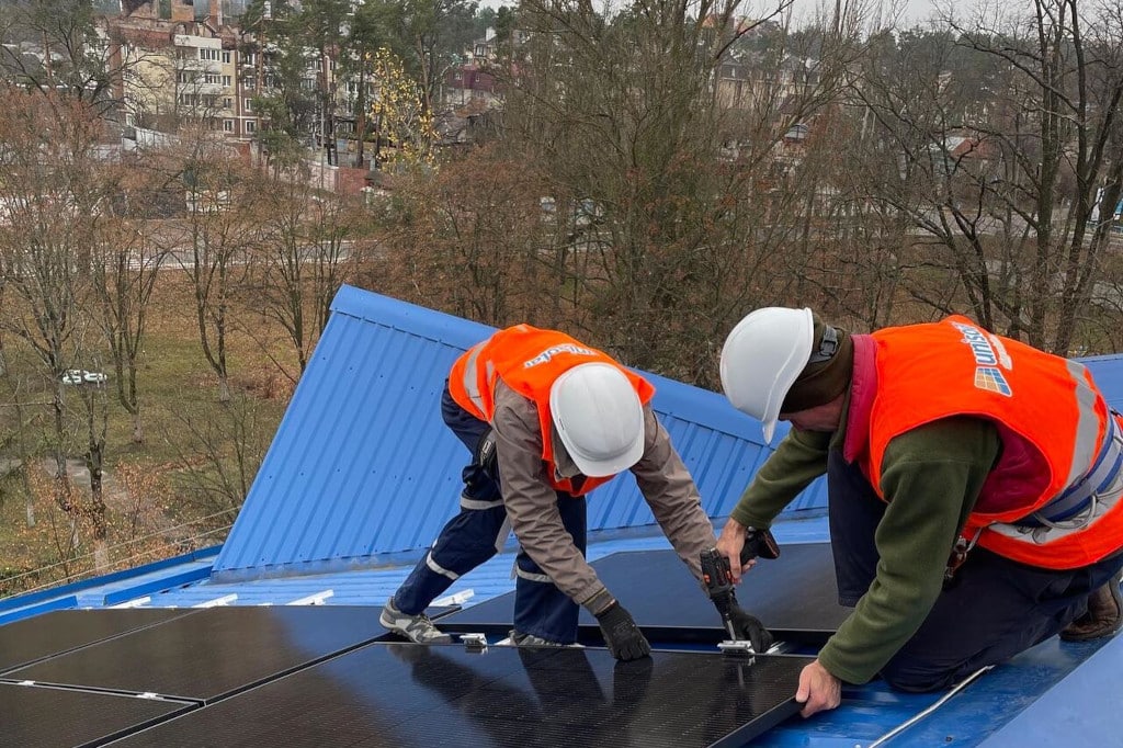 Zwei Personen installieren eine Photovoltaikanlage auf einem Schuldach in der Ukraine