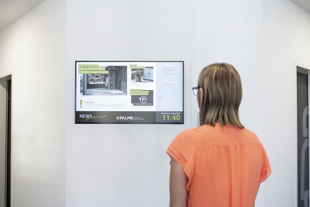 Digitale Mitarbeiter:innen-Information an der Wand auf Display mit davorstehender Person