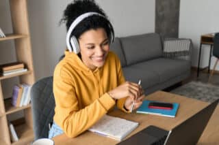 Studium von Zuhause: Lachende Person mit Kopfhörern sitzt am Schreibtisch