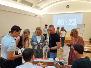 Gruppe mittelalter Menschen, teils Männer, teils Frauen, steht um einen Tisch