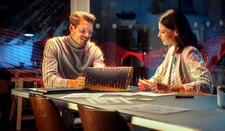 Zwei lächelnde junge Menschen vor einem Laptop