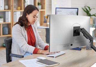 Frau sitzt am Schreibtisch vor einem Monitor und tippt auf der Tastatur