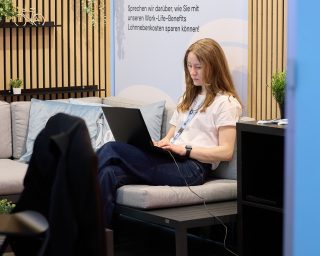 Junge Frau mit roten Haaren am Laptop auf dem Bett