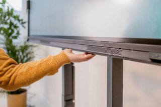 Hand eines Mannes berührt die Steuerung an der Unterseite eines Monitors.