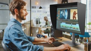 Mann in blauer Jeansjacke vor dem Monitor mit Audio-Bearbeitung auf dem Bildschirm
