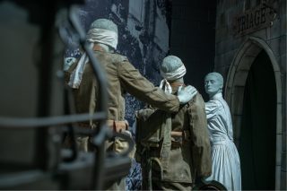 Ein Soldan aus dem 1. Weltkrieg berührt einen anderen vor ihm an der Schulter, beobachtet von einer Frau