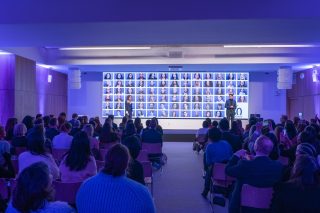 LED-Wand in Saal mit Menschen zeigt zahlreiche Porträts