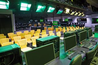 e-Sport-Arena mit diversen Bildschirmen an der Decke, gelben Stühle und grünen Tischen
