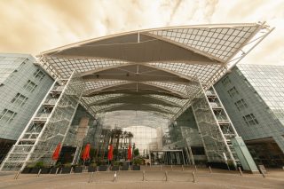 Das Bild zeigt den imposanten Eingangsbereich des Hilton Munich Airport mit seiner markanten Stahl-Glas-Konstruktion