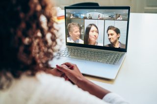 Frau mit Kopfhörer von hinten gesehen blickt auf Notebook mit Video-Konferenz