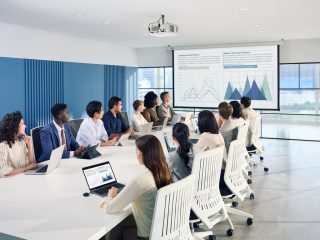 Besprechungstisch mit vielen Menschen. Ein Projektor zeigt ein Chart