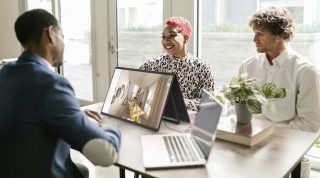 Drei junge Menschen an einem Tisch mit Monitor vor sich