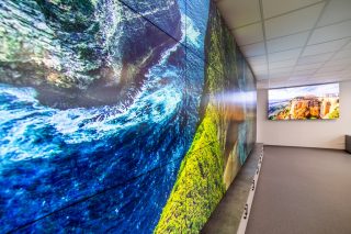 Schräge Ansicht einer Videowand aus mehreren Displays mit einem formatfüllenden Landschaftsbild, im Hintergrund ein weiterer Bildschirm an der Wand.