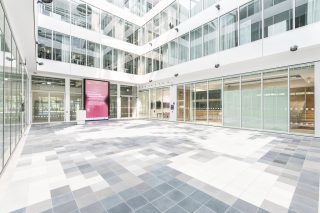 Helles Atrium des Cyber Valley I in Tübingen mit großformatiger Digital-Signage-Anzeige und angrenzenden verglasten Hörsälen.