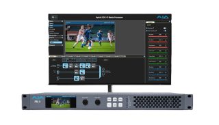 Ein Monitor zeigt die Weboberfläche des AJA FS8 mit Videovorschau einer Fußballszene und Farbkorrekturreglern, davor das Gerät im 19-Zoll-Format mit Frontdisplay und Bedienknöpfen