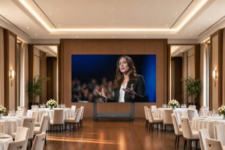 Große mobile LED-Wall von ViewSonic mit Rednerin auf dem Display in einem mit Tischen und Stühlen ausgestatteten Veranstaltungssaal.