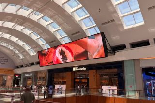 Großes querformatiges LED-Display unter einem gewölbten Glasdach in der Dubai Mall, darunter die Ladenfront einer Buchhandlung auf der Galerieebene
