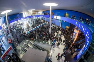 Blick von oben in die Eingangshalle der ISE 2026 in Barcelona mit Besucherströmen, Rolltreppen und umlaufendem LED-Band mit der Aufschrift „Digital Signage + DOOH – Hall 4