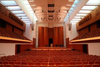 Blick aus dem Zuschauerraum auf die Bühne des Rolf Böhme Saals im Konzerthaus Freiburg. Links und rechts der Bühne hängen die beiden Line-Array-Lautsprechersysteme