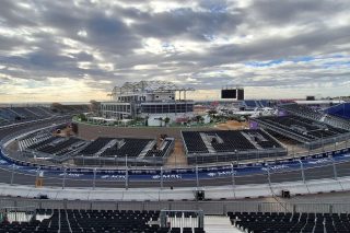 Panoramablick über den MADRING in Madrid mit Tribünen, einer Kurve der Rennstrecke und einem mehrstöckigen Hospitality-Gebäude unter bewölktem Himmel