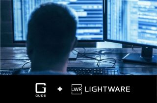 Person von hinten vor zwei Monitoren mit Codezeilen, darunter die Logos von GUDE und Lightware