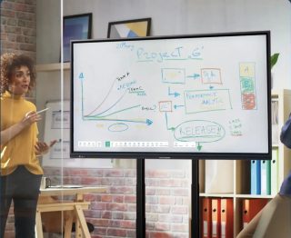 Screenshot der neuen heinekingmedia-Website im dunkelblauen Corporate Design, daneben ein interaktives Display auf einem Rollständer mit handschriftlichen Notizen, davor eine Frau mit Displaystift