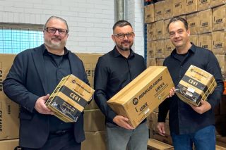 Drei Mitarbeiter in einem Lager mit Kartons von Renkus-Heinz und verpackten Lautsprecherprodukten.